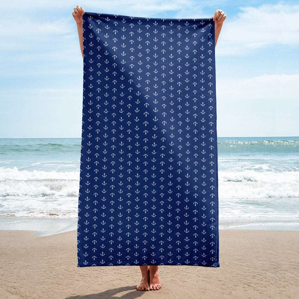 woman holding up over-sized navy beach towel with anchors at ocean